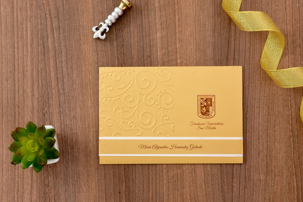 Invitación de grado dorada con arabescos en relieve y faja blanca