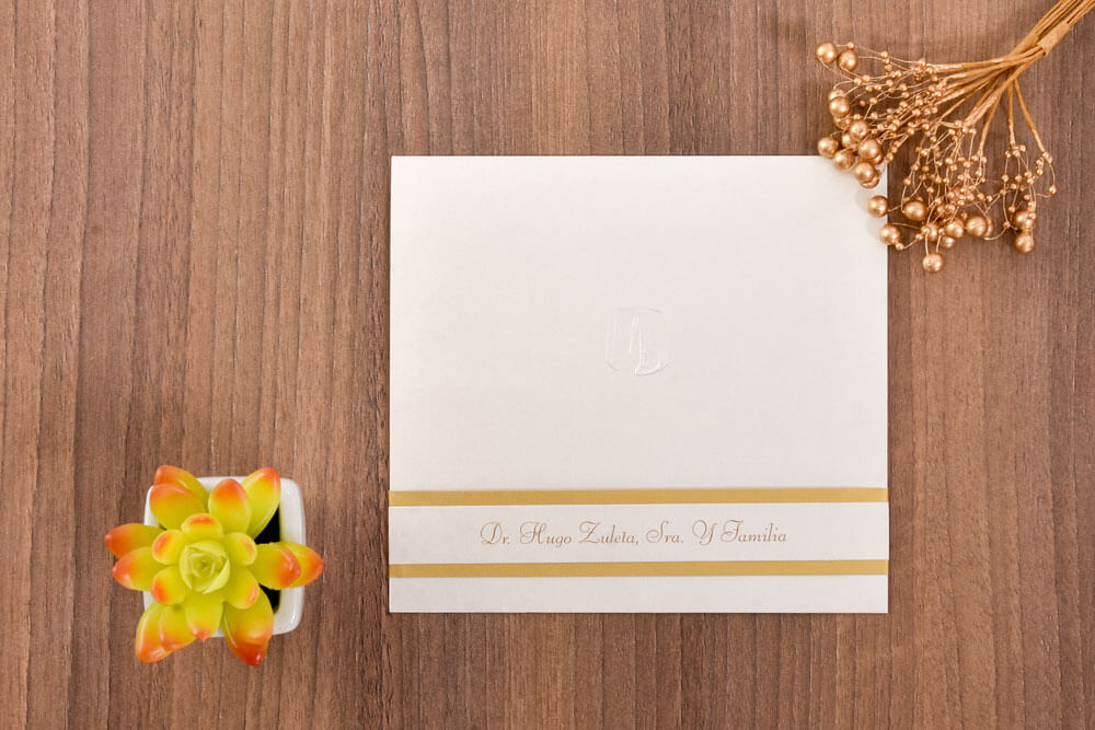 Invitación de grado blanca con monograma en relieve y faja dorada