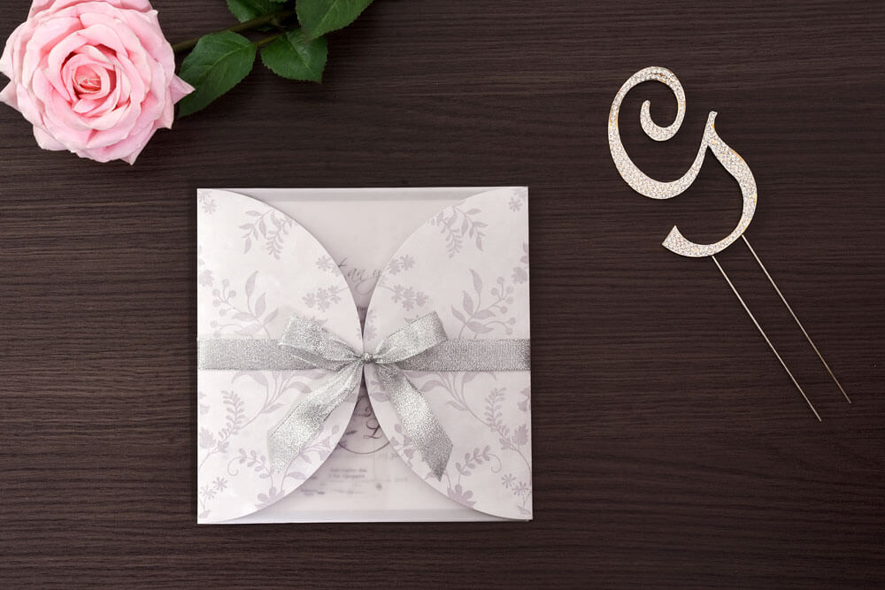 Invitación de matrimonio con follaje impreso y lazo plateado